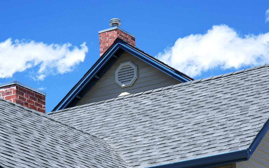 Gray shingled house roofs and gables under a blue sky with scattered clouds
