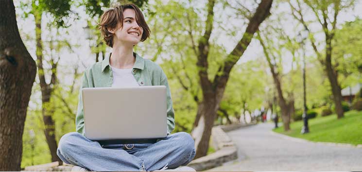 Person sitting cross-legged on a park bench working on a laptop - https://www.amherstins.com/