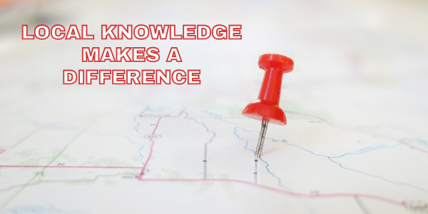 A close-up photograph of a paper map with a red pushpin stuck into it, positioned slightly right of center.