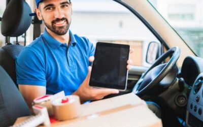 A smiling man inside a car, holding a tablet and looking at the camera